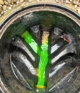 A close-up of a blocked drain with green dye to identify leaks or blockages.